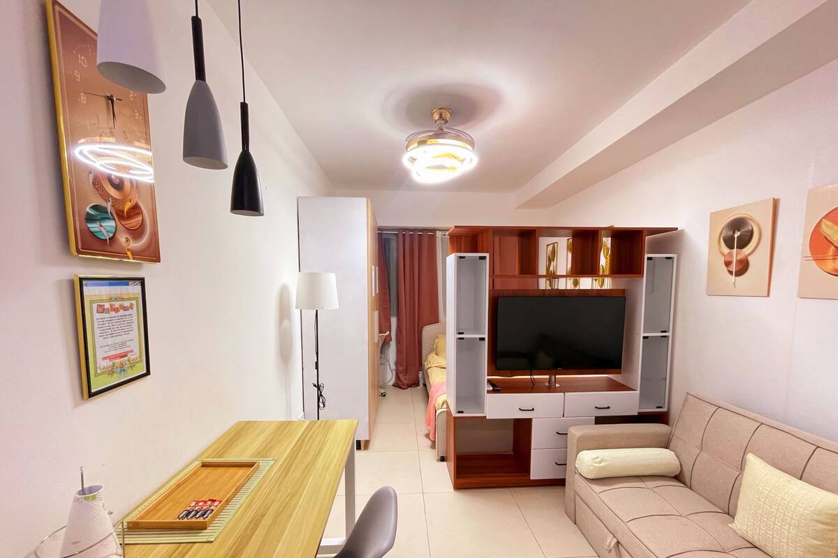 A modern living room with a wooden dining table, a sofa, a TV, and a ceiling fan.