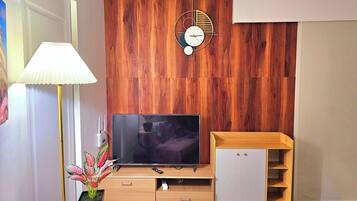 A modern living room with a wooden wall panel, a flat-screen TV, a wooden cabinet, a lamp, and a clock.