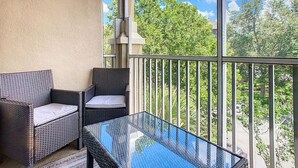 Un balcón con mobiliario de mimbre y una mesa de vidrio, con vistas a un paisaje verde.