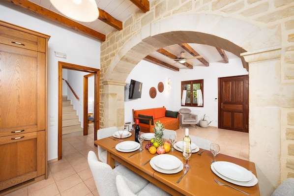 A dining area with a wooden table set for four, a stone archway, a wooden staircase, and a stone wall.