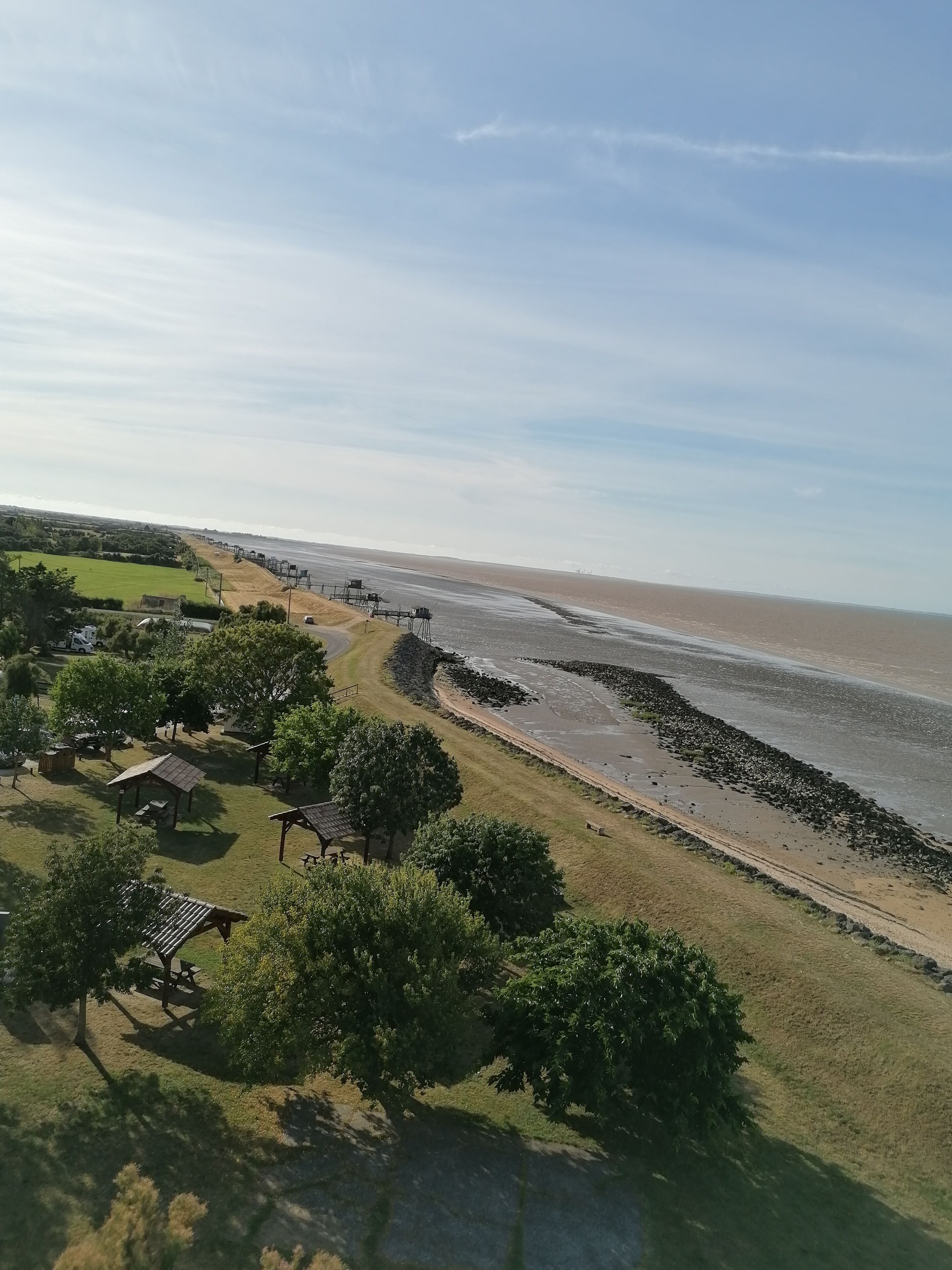 A coastal area with a sandy beach, picnic areas, and a clear sky.