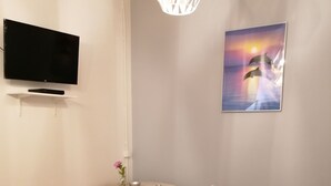 Una sala de estar moderna con un televisor de pantalla plana, una mesa de comedor con sillas, un sofá con cojines y un aplique de pared.