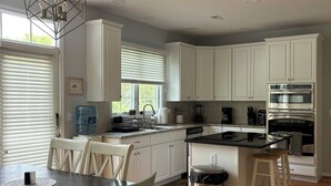 A modern kitchen with white cabinets, a central island with stools, a built-in oven, and a hanging light fixture.