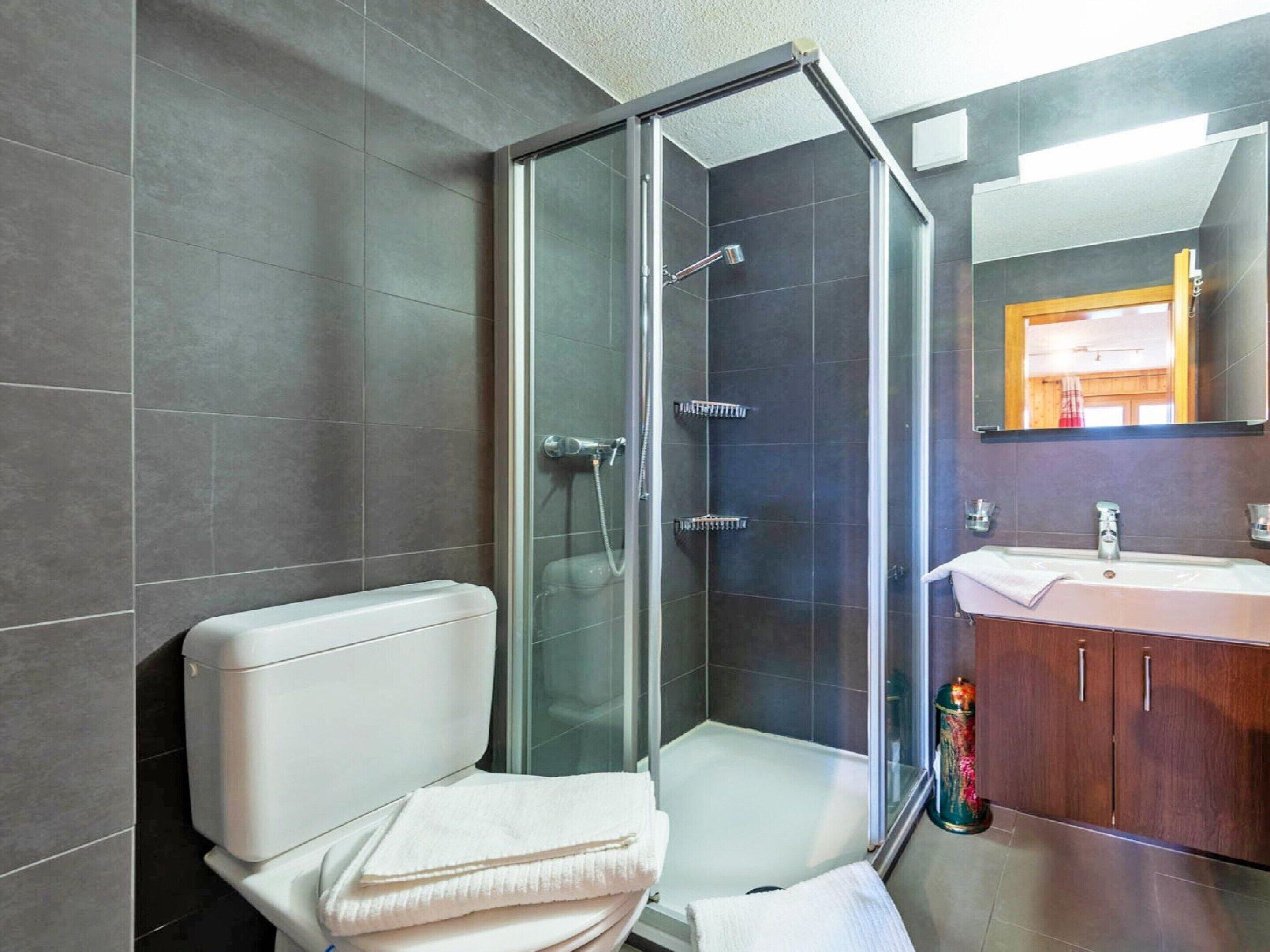 Un baño moderno con ducha de vidrio, inodoro y lavamanos con mueble de madera.