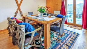 A dining area with a wooden table set for four, a large window with a view, and a rustic chair with a blue cushion. - Chalet in Les Collons by Ski Slope (Vex)