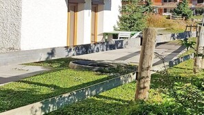 A two-story building with a balcony, a small garden area, and a view of a forested area in the background. - Chalet in Les Collons by Ski Slope (Vex)