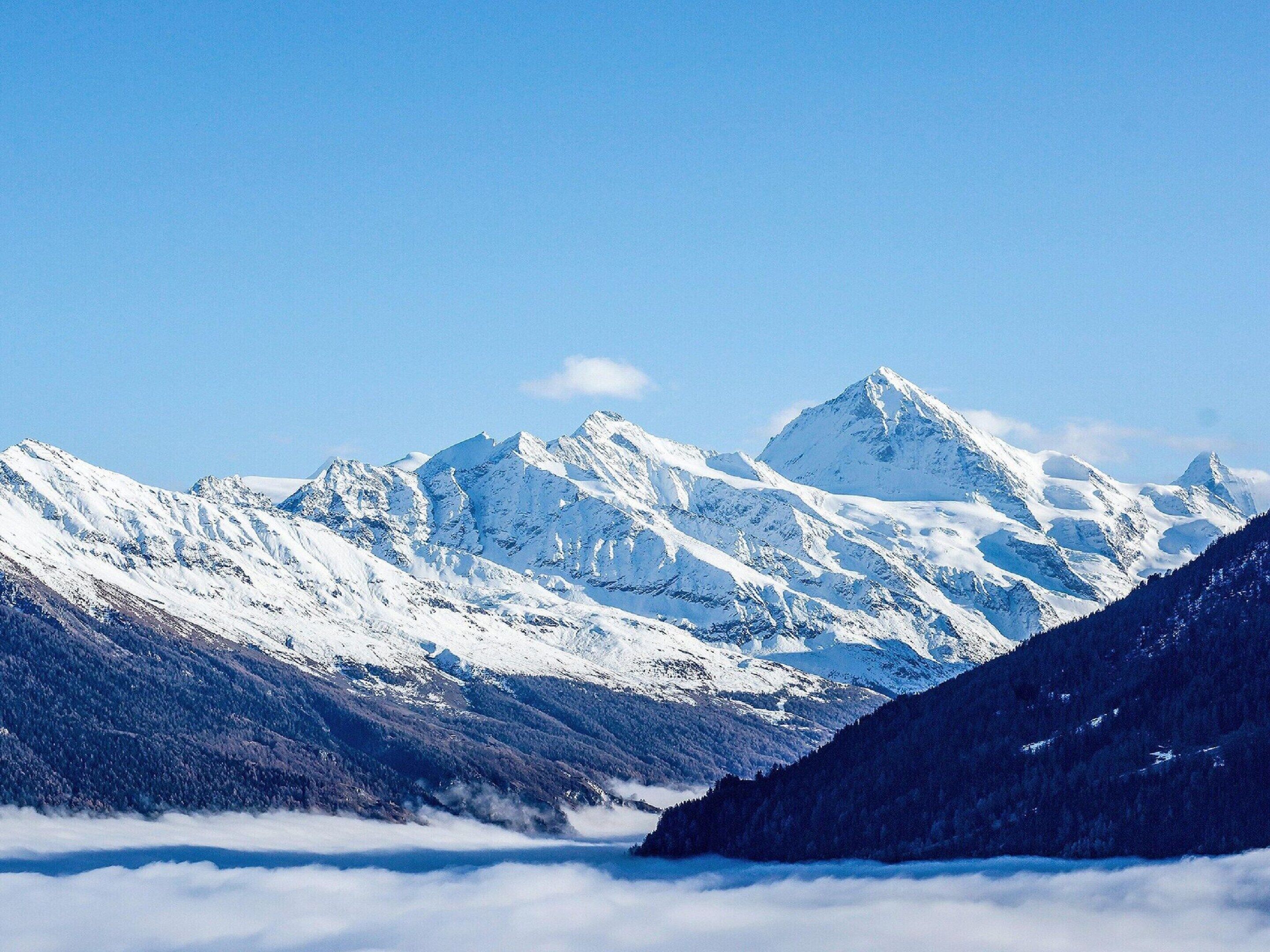 Un paysage de montagne avec des sommets enneigés et une vallée en contrebas.