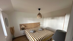 Un dormitorio con una cama a rayas, una mesita de noche, una lámpara, un espejo y una lámpara colgante.