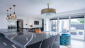 Une cuisine moderne avec un îlot central en marbre noir, un lustre et une vue sur la terrasse extérieure.