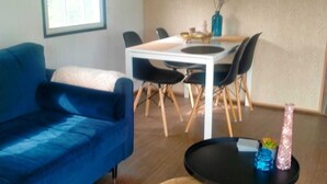 A modern living room with a blue sofa, a dining table with chairs, and a small round table with decorative items. - Chalet Vienna (Menaam)