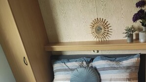 A bedroom with a bed, striped bedding, a round blue pillow, a wall clock, and a shelf with a potted plant. - Chalet Vienna (Menaam)