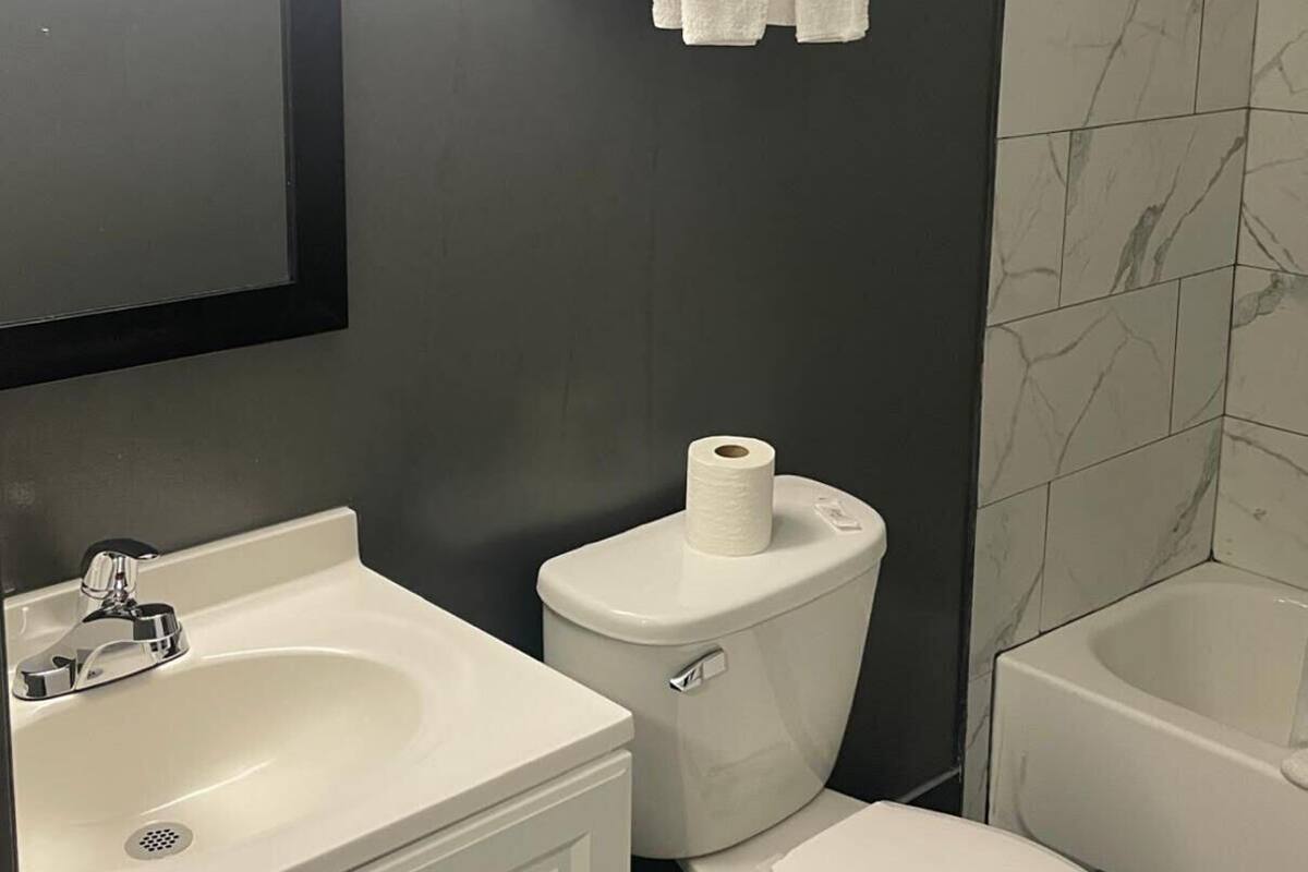 A bathroom with a white sink, toilet, and bathtub. There is a mirror above the sink and a towel rack with towels above the toilet.