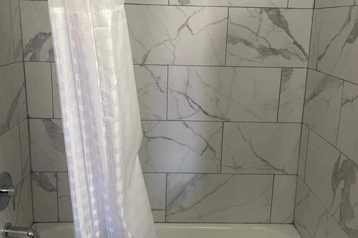 A bathroom with a bathtub, a shower curtain, and marble-patterned tiles.