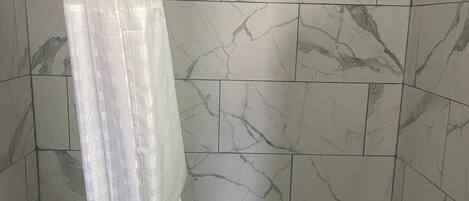 A bathroom with a bathtub, a shower curtain, and marble-patterned tiles.