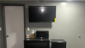A room with a flat-screen TV mounted on the wall, a small black refrigerator, and a black entertainment unit with a microwave. - Travelers Rest Motel (Birmingham)