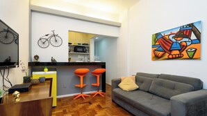 A modern living room with a grey sofa, wooden flooring, and a kitchen area in the background. - BR-96 (Rio de Janeiro)