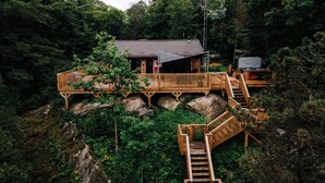 Una cabaña de madera con terraza y escaleras, rodeada de un bosque denso.