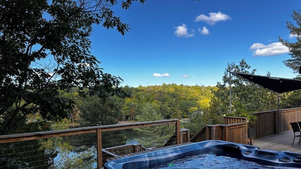 Un jacuzzi en una terraza de madera con vista a un lago y un bosque.