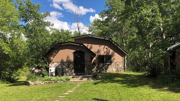 A rustic cabin with a stone foundation, a wooden exterior, and a black front door. - Glacier National Park central location. Many Glacier, St. Mary, and Two Medicine (Babb)