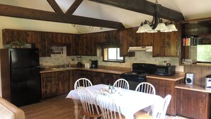A kitchen with wooden cabinets, a black refrigerator, a dining table with chairs, and a hanging light fixture. - Glacier National Park central location. Many Glacier, St. Mary, and Two Medicine (Babb)
