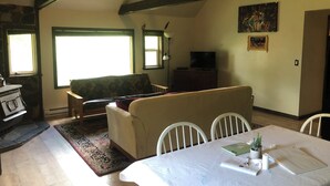 A cozy living room with a sofa, a dining table set with a laptop, and a TV on a wooden cabinet. - Glacier National Park central location. Many Glacier, St. Mary, and Two Medicine (Babb)