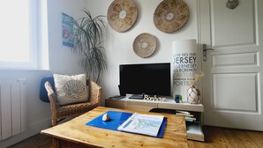 Una sala de estar con televisor, una mesa de centro con un libro, una planta y decoración en la pared.