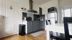 Una cocina compacta con puerta blanca, gabinetes grises, un cesto de basura negro, un microondas y un refrigerador pequeño.