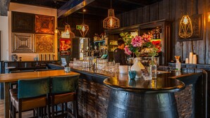 A bar area with a counter, stools, and hanging lights. There are decorative elements on the wall and a person working behind the bar. - Modern Holiday Home Near Golf Course (Velsen-Zuid)