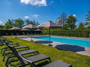 A swimming pool with lounge chairs and umbrellas, surrounded by a hedge and trees.