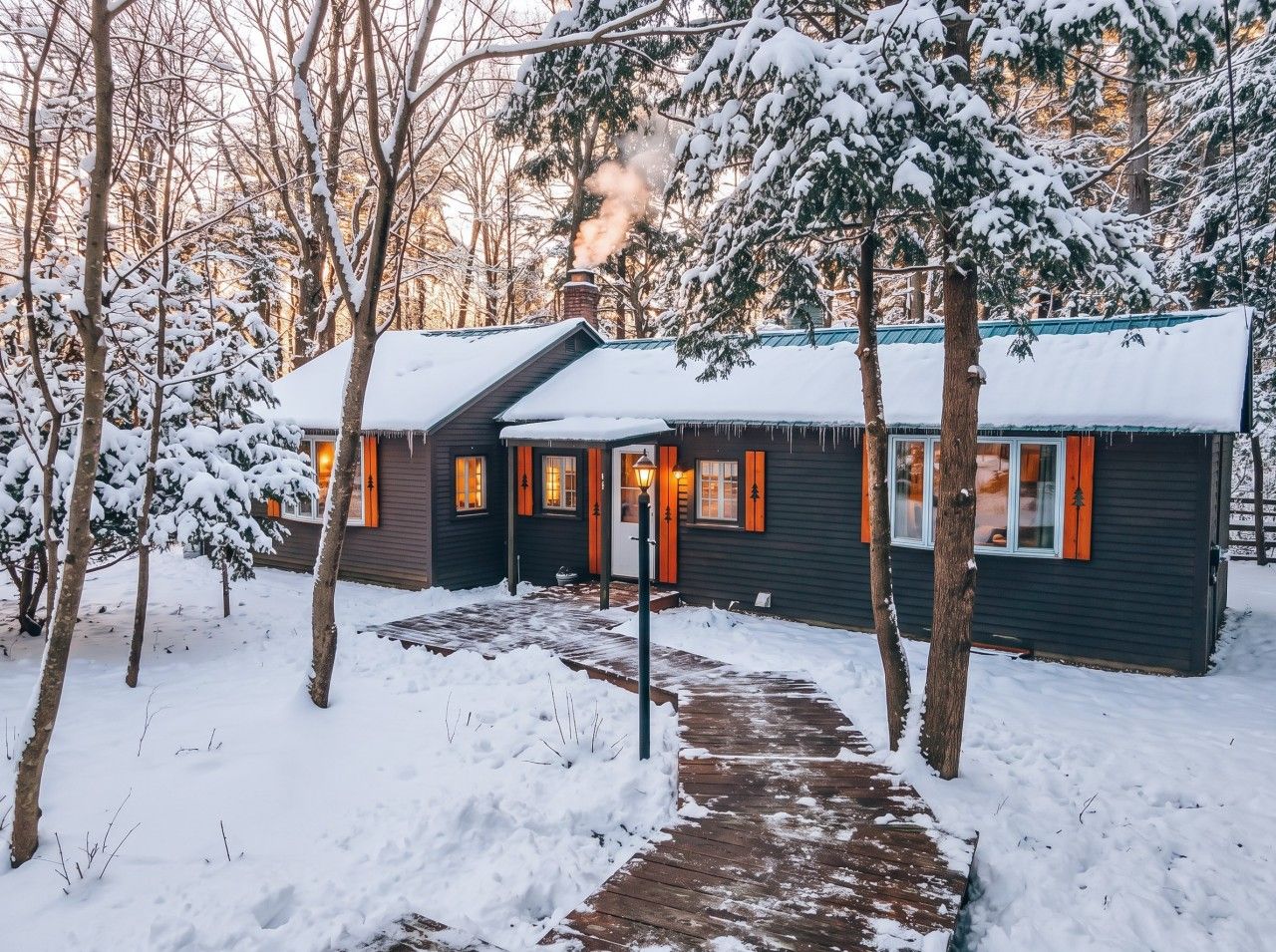 A cabin with a snow-covered roof, a chimney, and a pathway leading to the entrance.