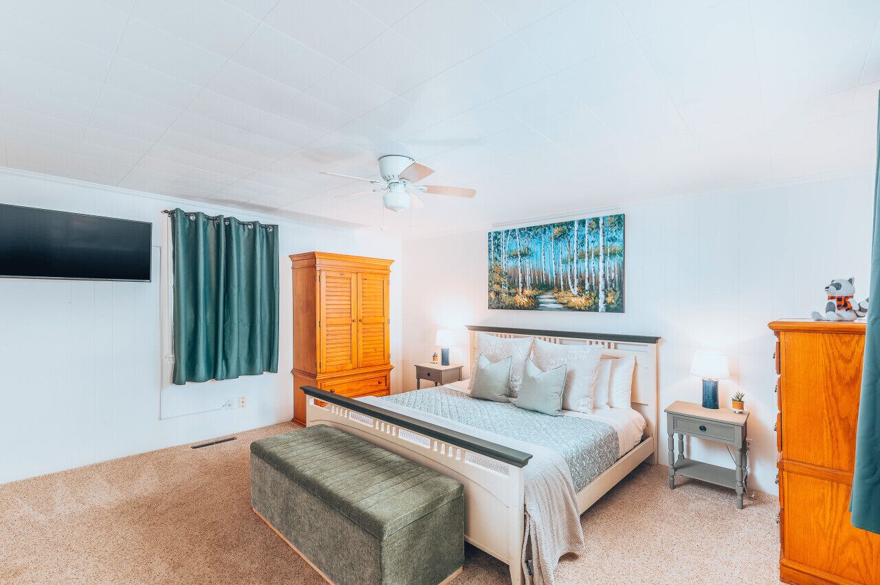 Una camera da letto con un letto, un comodino, un armadio in legno, una panca, una ventola a soffitto e un quadro appeso al muro.