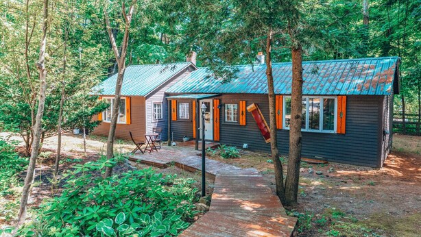 Une cabane avec un toit en métal, entourée d’arbres et dotée d’une terrasse en bois.