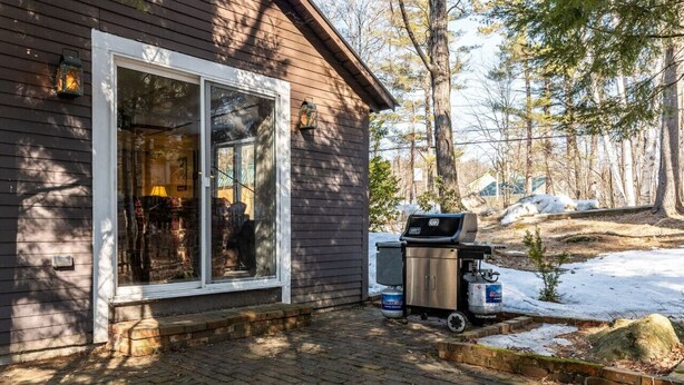 Une cabane avec une grande fenêtre, un barbecue à l’extérieur et un sol recouvert de neige.
