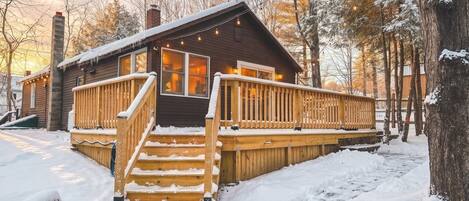 A cabin with a wooden deck, a staircase, and a snow-covered landscape.