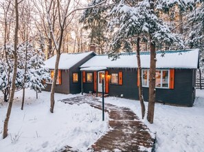 A cabin with a snow-covered roof, a wooden deck, and a pathway leading to the entrance. - Cozy dog friendly cabin moments from Cranmore/NOCO (Conway)