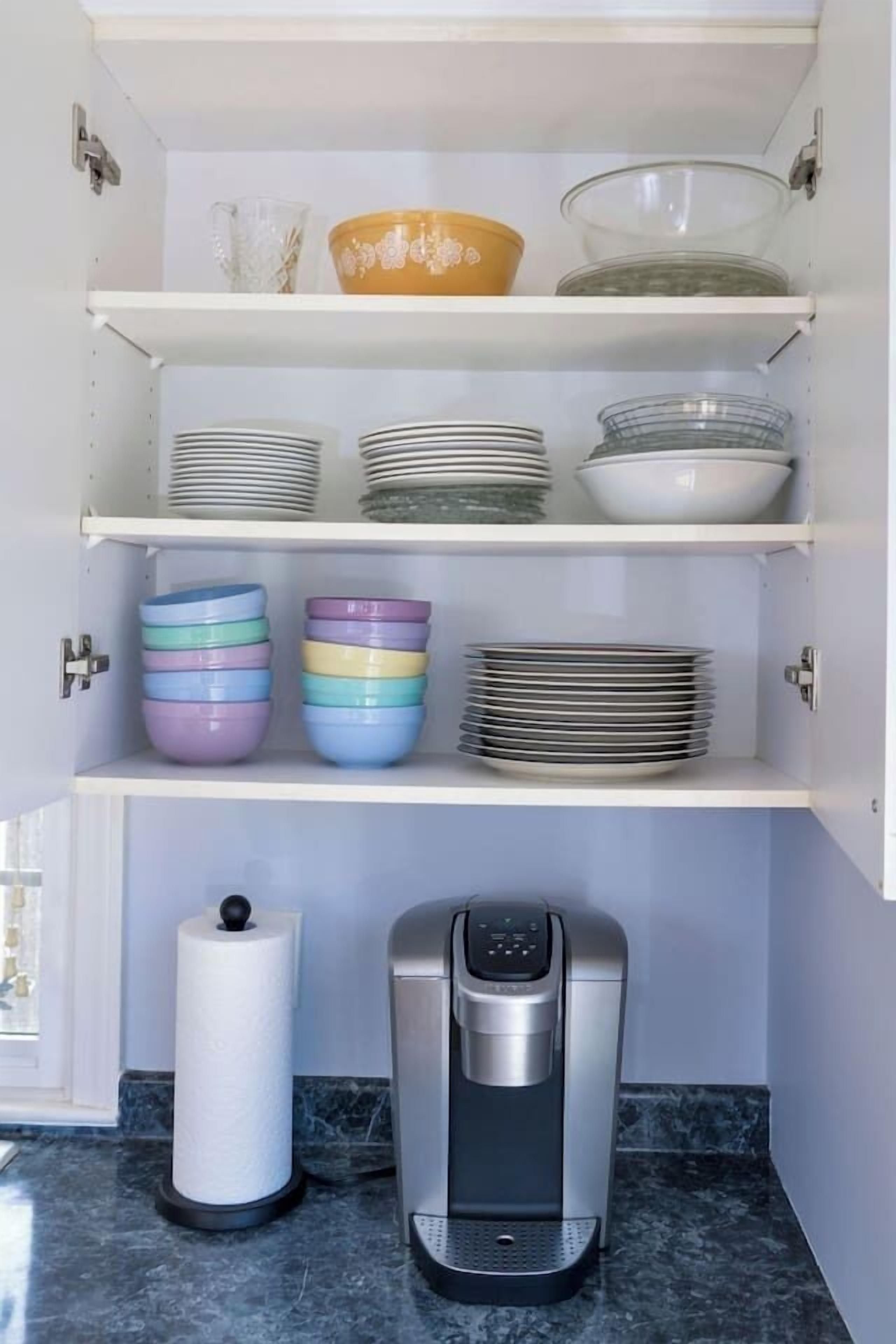 Een keuken met witte planken waarop kommen en borden staan, een keukenrolhouder en een koffieapparaat.