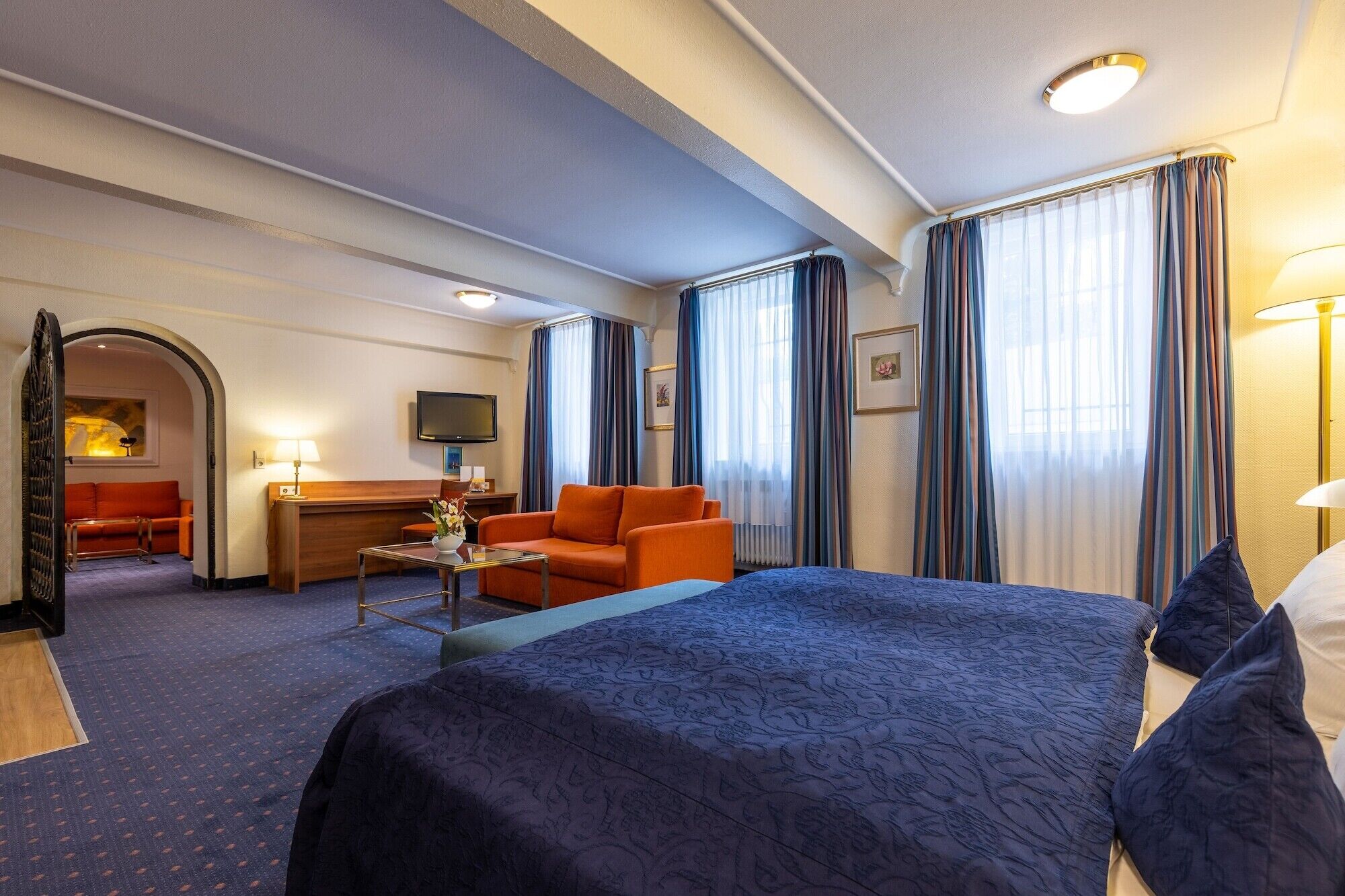 A hotel room with a large bed, a desk with a chair, a sofa, and a TV.