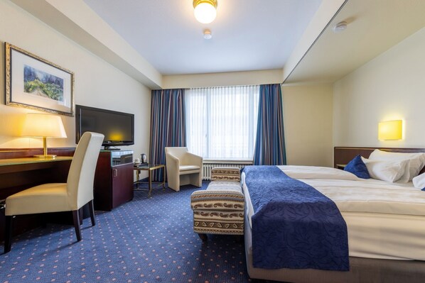 A hotel room with two beds, a desk with a chair, a television, and a window with curtains. - Trip Inn Hotel Uebachs (Düsseldorf)