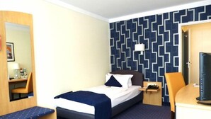 Quarto de hotel com uma cama, uma secretária com cadeira, uma televisão e um papel de parede estampado.