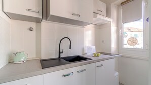 A modern kitchen with white cabinets, a black sink, and a window with a view of buildings.