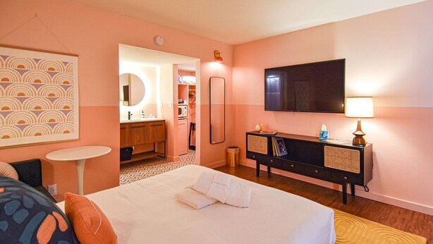 Ein Hotelzimmer mit einem großen Bett, einem Nachttisch, einem an der Wand montierten Fernseher, einem Spiegel und einem kleinen Beistelltisch.