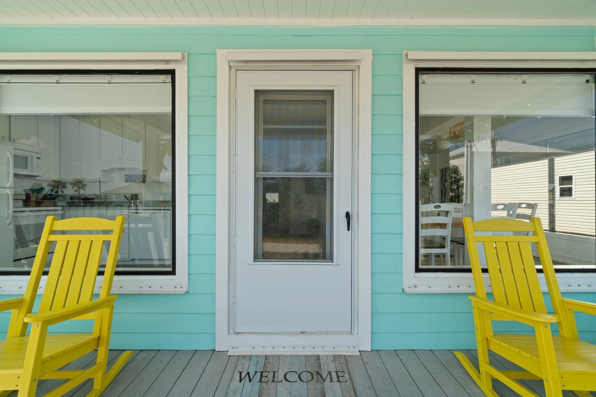A turquoise house with a white door and two yellow rocking chairs in front.