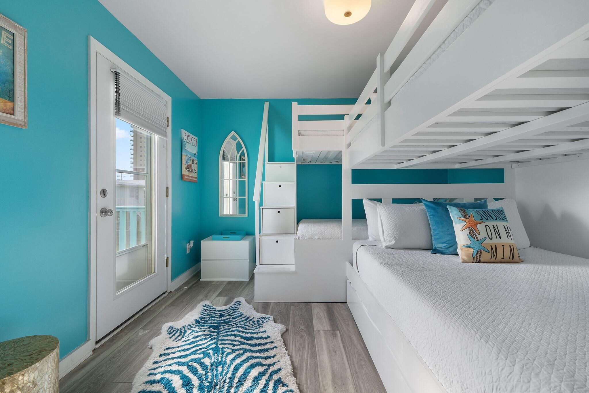 A bedroom with a bunk bed, a white dresser, a nightstand, a mirror, and a window with blinds.