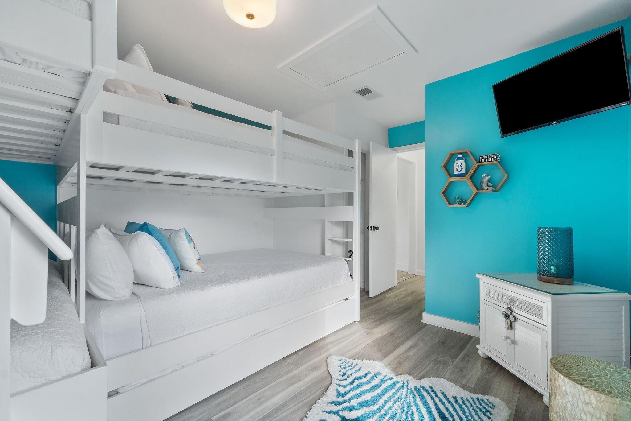 Une chambre avec un lit superposé, un mur d’accent de couleur turquoise, un téléviseur à écran plat et un petit meuble de rangement.