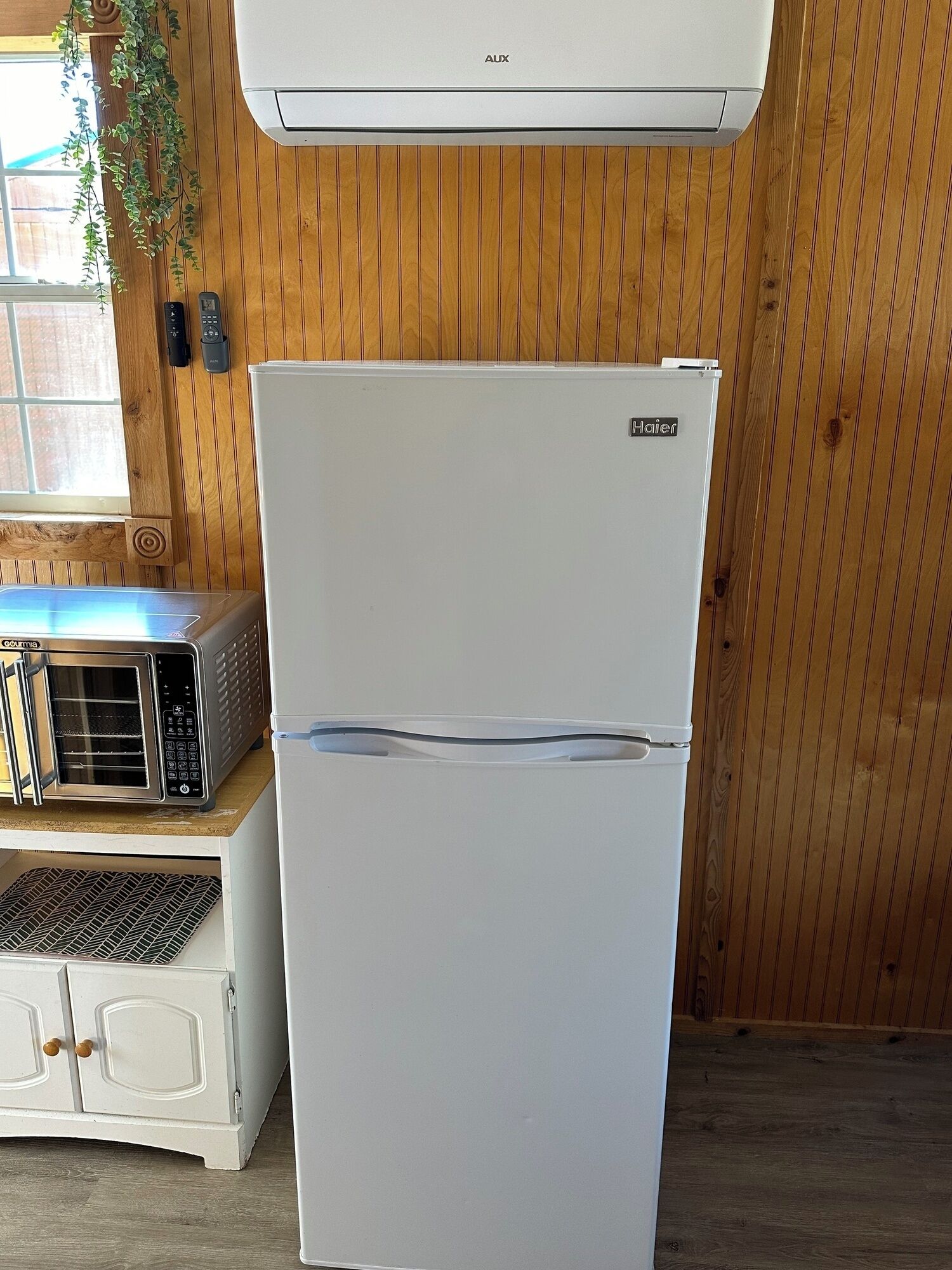A white refrigerator with a Haier logo, a microwave, and a small oven on a wooden countertop.