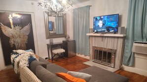 Een woonkamer met een grijze bank, een salontafel, een televisie, een open haard en een kroonluchter.