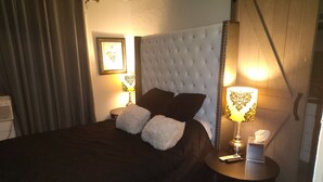 Een hotelkamer met een groot bed, twee bedlampen, een nachtkastje met een zakdoosje en een lijst aan de muur.