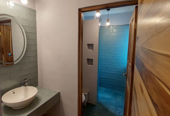 Un baño con un lavabo redondo, un espejo y una ducha con azulejos azules.