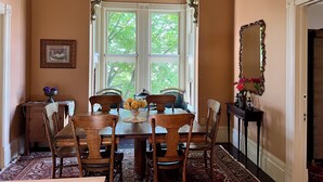 Ein Esszimmer mit großem Fenster, aufwendiger Decke und Spiegel an der Wand.