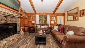 Un salon chaleureux avec une cheminée en pierre, des poutres apparentes en bois et un canapé en cuir marron.